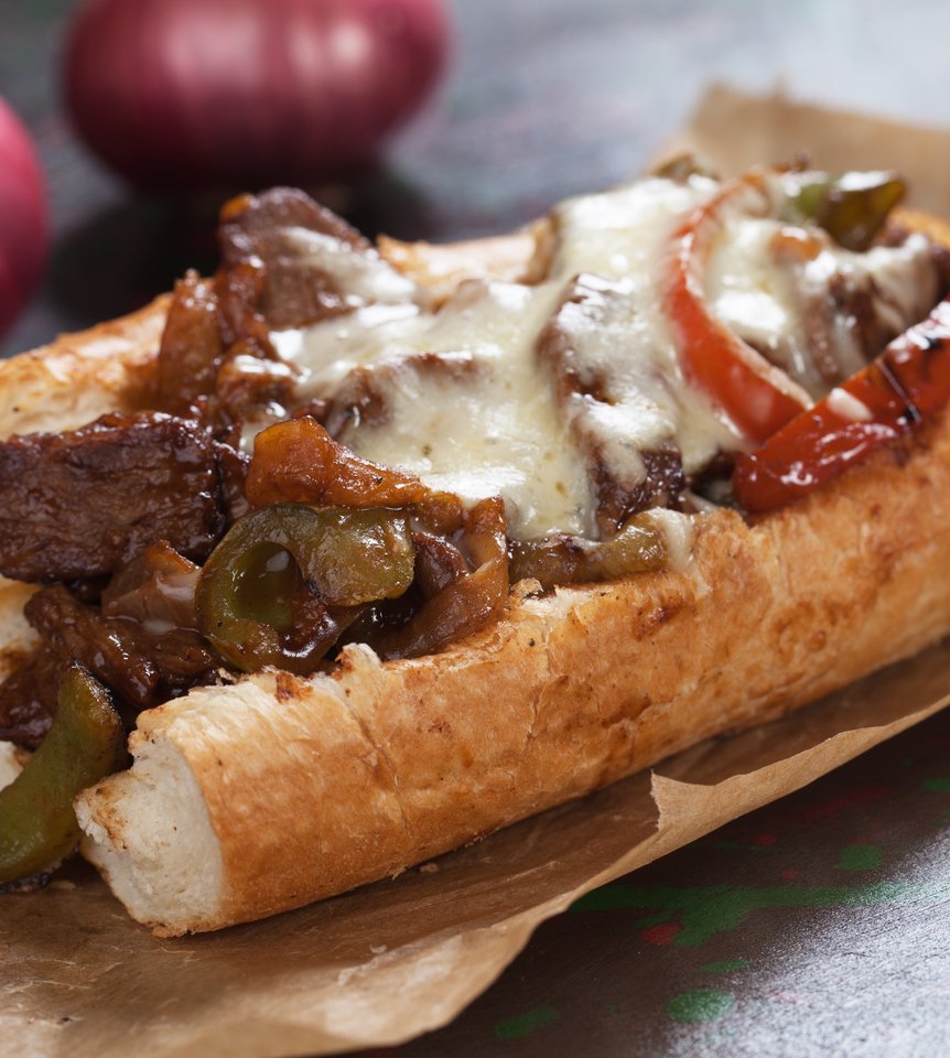 Philly Cheese Steak on brown paper with onions in the background