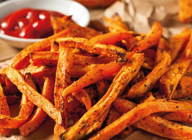 Sweet potato fried piled up with a pot of ketchup in the background