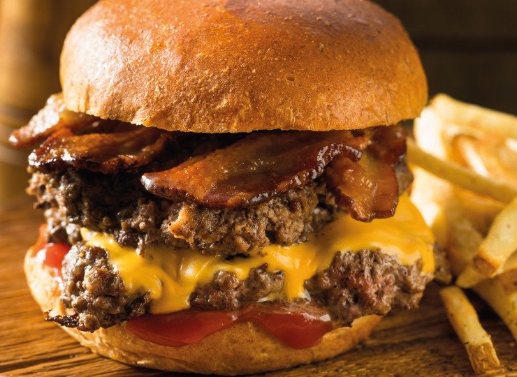 Close up of a double smash beef burger with crispy turkey bacon with fries on the side